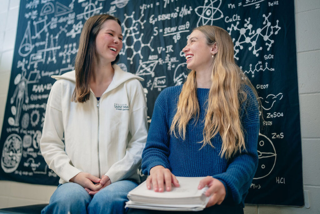 Two students in front of black science tapestry wall decor laughing together.