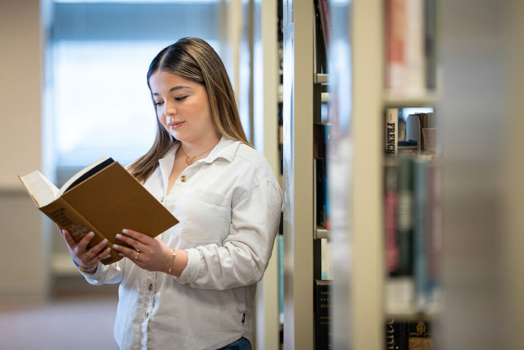 Student reading a book between library stacks.