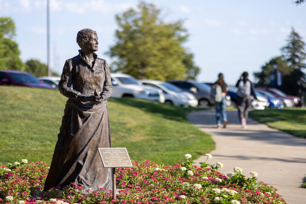 Statue of Sister Catherine Mcauley in garden bed with two students walking in the background