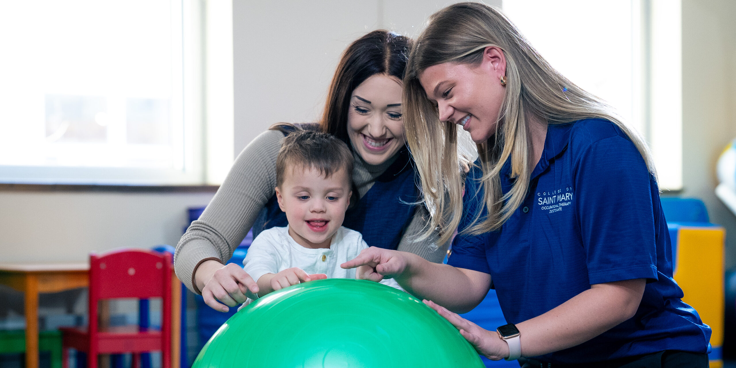 A College of Saint Mary faculty member works with an occupational therapy doctorate student and a child, teaching OT skills.