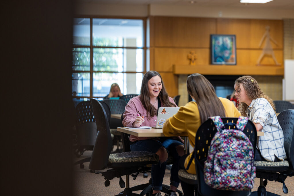 Three students studying together at a table in a campus library.
