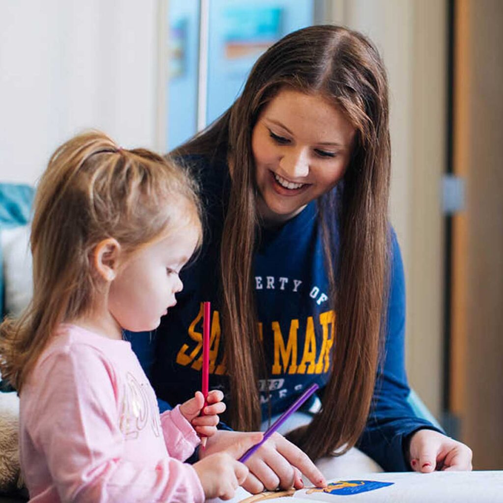 A mother and child at a table drawing and doing crafts with markers