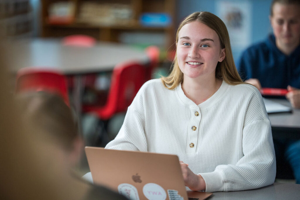 Education student listens attentively while working on a laptop in a classroom.